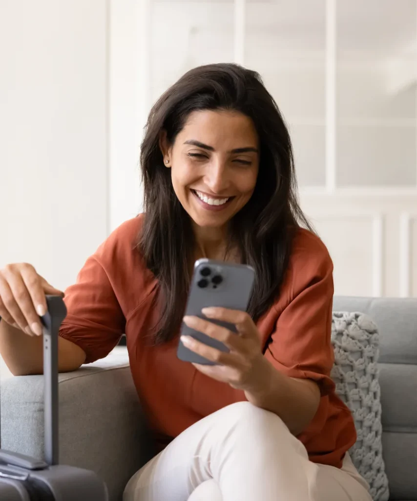 Woman smiling on the couch using the cell phone and a laptop.